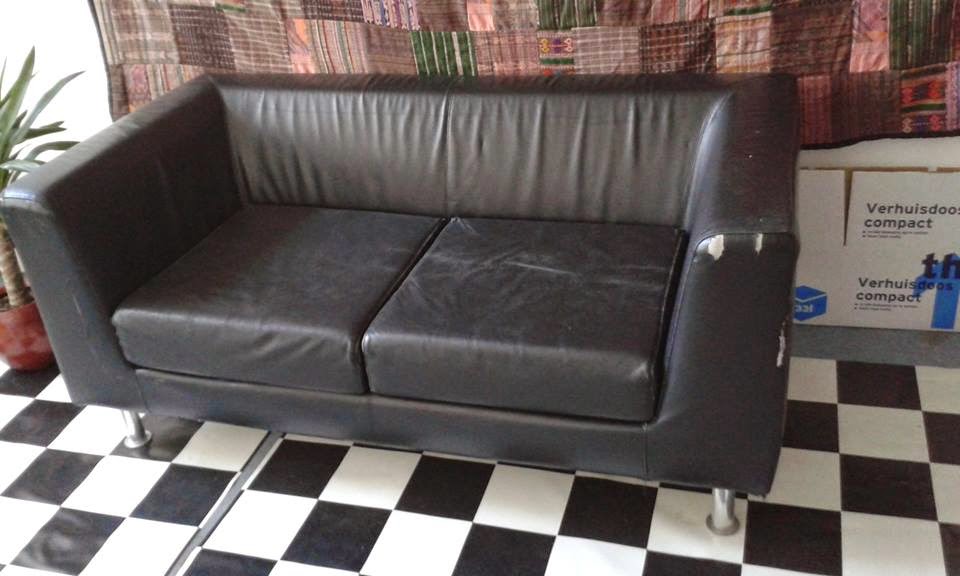 Black couch in a room surrounded by a house pland and a folded moving box.